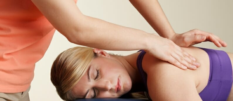 A woman lying down and getting her shoulders massaged. Looking for a student Massage clinic? Call AMBI.
